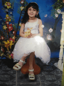 a little girl in a white dress sits on a stool