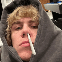 a man with a hoodie on has a cigarette in his nose