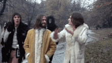 a group of people wearing fur coats are walking down a path in a park .