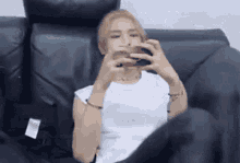 a woman is sitting on a couch eating a hamburger while looking at her phone .