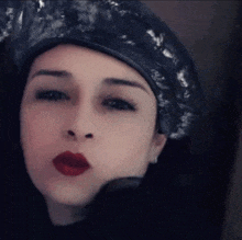 a woman wearing a black hat and red lipstick is making a kiss .