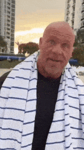 a bald man with a striped towel around his neck is standing on a beach .