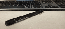 a black ink pen with a barcode on it sits on a desk in front of a keyboard