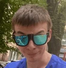 a young man wearing a blue shirt and sunglasses is making a funny face .