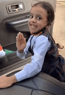 a little girl is sitting in the back seat of a car and waving