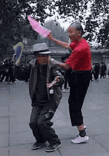 a man in a red shirt is standing next to a man in a hat holding a pink feather .