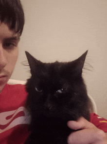 a man holding a black cat with a red nike shirt on