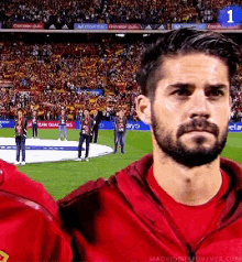 a man in a red shirt stands on a soccer field in front of a crowd with the number 1 visible