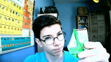 a boy wearing glasses is holding a bag of food in front of a periodic table of elements