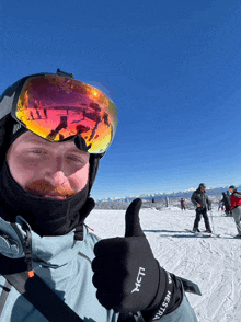 a man wearing ski goggles and a glove that says mcti gives a thumbs up