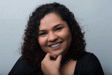 a woman with curly hair has her hand on her chin and smiles