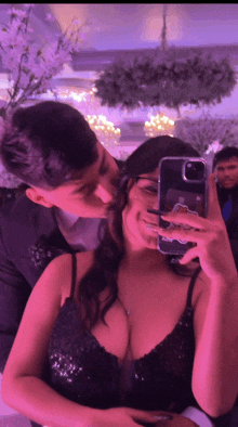 a man kissing a woman on the cheek while she takes a selfie