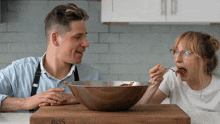 a man and a woman are eating from a bowl on a wooden cutting board that says boos on it