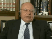 a man in a suit and tie is sitting in front of a bookshelf with books on doerr medicine on it