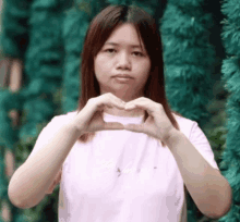 a woman is making a heart shape with her hands in front of a green background .