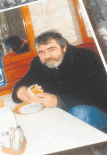 a man with a beard sits at a table with a plate of food