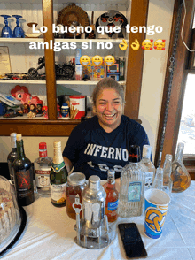 a woman wearing a shirt that says inferno sits at a table with bottles of alcohol