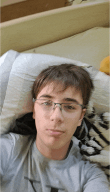 a young man wearing glasses is laying on a bed with a pillow