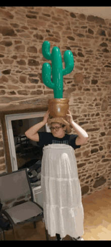 a person wearing a white dress and a cowboy hat is holding an inflatable cactus on top of their head