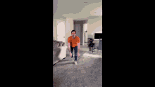 a man in an orange shirt and blue jeans is jumping in a living room