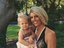 a woman is holding a little girl in her arms and she is wearing a black tank top with a floral design