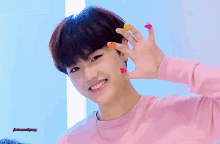 a young boy wearing a pink sweater and a necklace is smiling and holding up his hand with hearts painted on it .