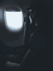 a man looks out of an airplane window while holding a cup