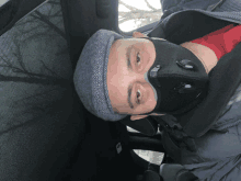 a man wearing a black mask and a hat is laying in a car