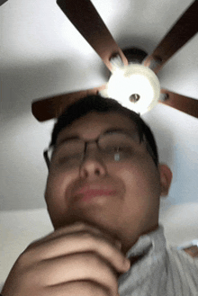 a man wearing glasses is standing under a ceiling fan