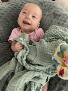 a baby wrapped in a green blanket smiles at the camera