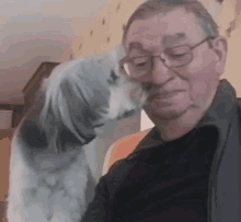 an older man with glasses is sitting in a chair with a dog licking his face .