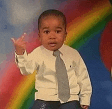 a young boy in a suit and tie is giving the middle finger in front of a rainbow background .