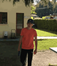 a man wearing an orange shirt and black pants is walking in front of a building with a sign pointing to the right