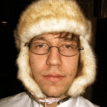 a man wearing glasses and a fur hat is looking at the camera