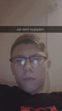 a young man wearing glasses is taking a selfie with the words jak debil wygladam