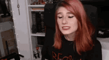 a woman with red hair is sitting in a chair in front of a shelf with books on it .