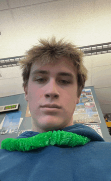 a young man holds a green worm around his neck in front of a sign that says dubai