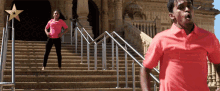 a woman in a pink shirt stands on a set of stairs next to a man in a red shirt