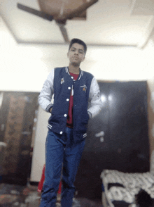 a young man wearing a blue and white varsity jacket stands in a dark room