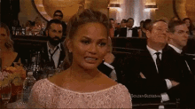 a woman in a pink dress is sitting in front of a crowd of people at a awards ceremony .