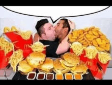 a couple of men kissing in front of a pile of hamburgers and french fries .