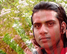 a man wearing headphones stands in front of a bush of flowers