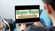 a man is typing on a laptop with a super royal electrolyte beverage on the screen