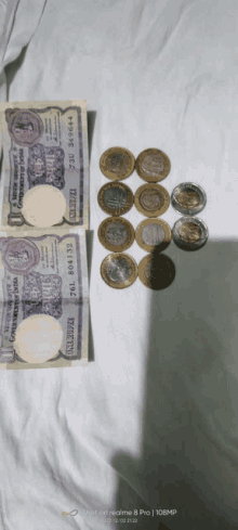 two 10 rupee bills and some coins are on a white surface