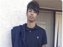 a young man wearing a blue polo shirt and a blue jacket is standing in front of a white wall .