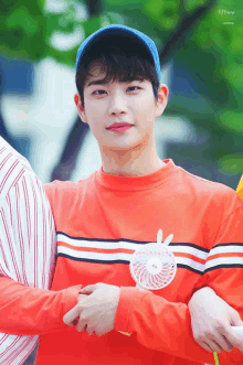 a young man wearing a red shirt and a blue hat holds a small fan