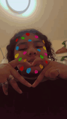 a girl with smiley faces on her face making a heart shape with her hands