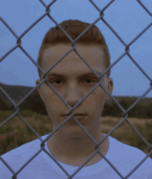 a young man behind a chain link fence looking at the camera