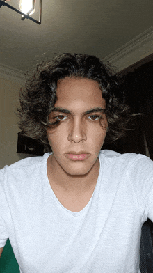 a young man with curly hair and a white shirt looks at the camera