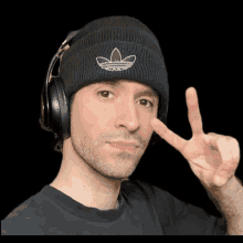 a man wearing a black beanie and headphones is giving a peace sign .